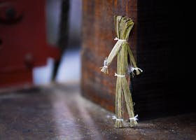 Close-up of an artistic handmade straw doll leaning against wood. Creative and decorative image.